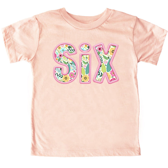 Close-up of floral SIX graphic on peach girls birthday shirt with pink embroidered-style lettering