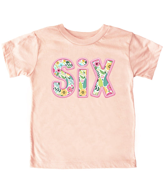 Close-up of floral SIX graphic on peach girls birthday shirt with pink embroidered-style lettering