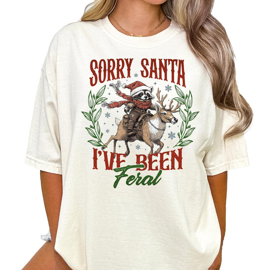 Front view of Sorry Santa I've Been Feral raccoon graphic Christmas shirt in seafoam green