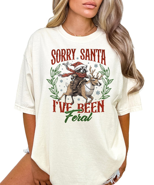 Front view of Sorry Santa I've Been Feral raccoon graphic Christmas shirt in seafoam green
