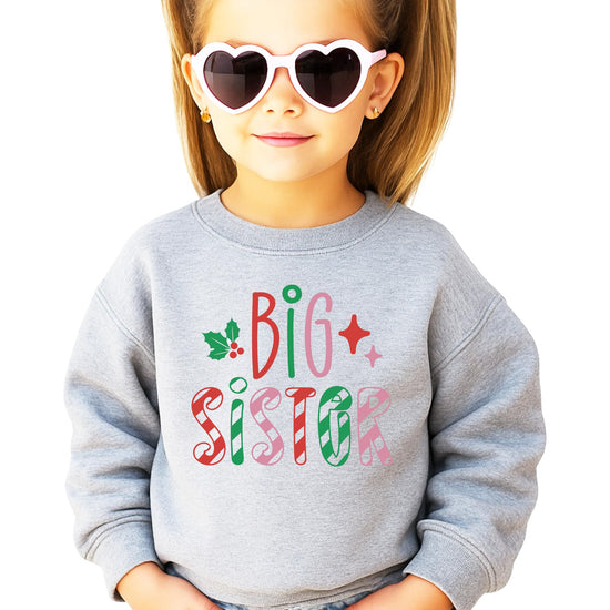 Close-up of Big Sister candy cane lettering with holly and star holiday accents on white sweatshirt