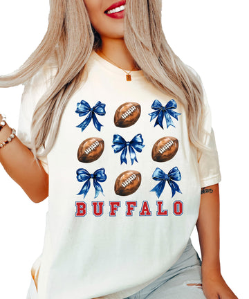 Ivory women's Buffalo football spirit tee with red lettering, footballs, and blue coquette bows graphic