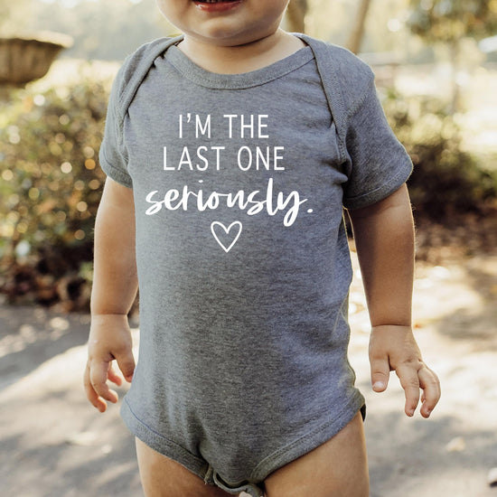 Baby bodysuit with humorous pregnancy announcement graphic, shown in multiple sizes for newborns