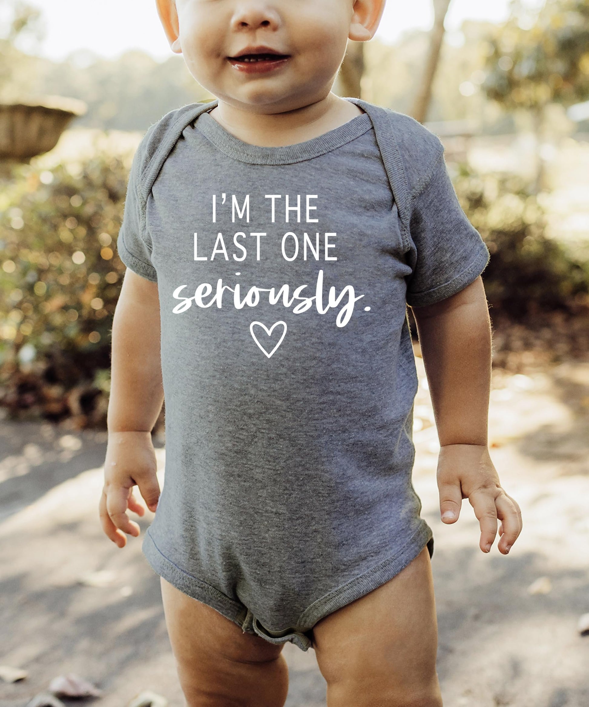 Baby bodysuit with humorous pregnancy announcement graphic, shown in multiple sizes for newborns