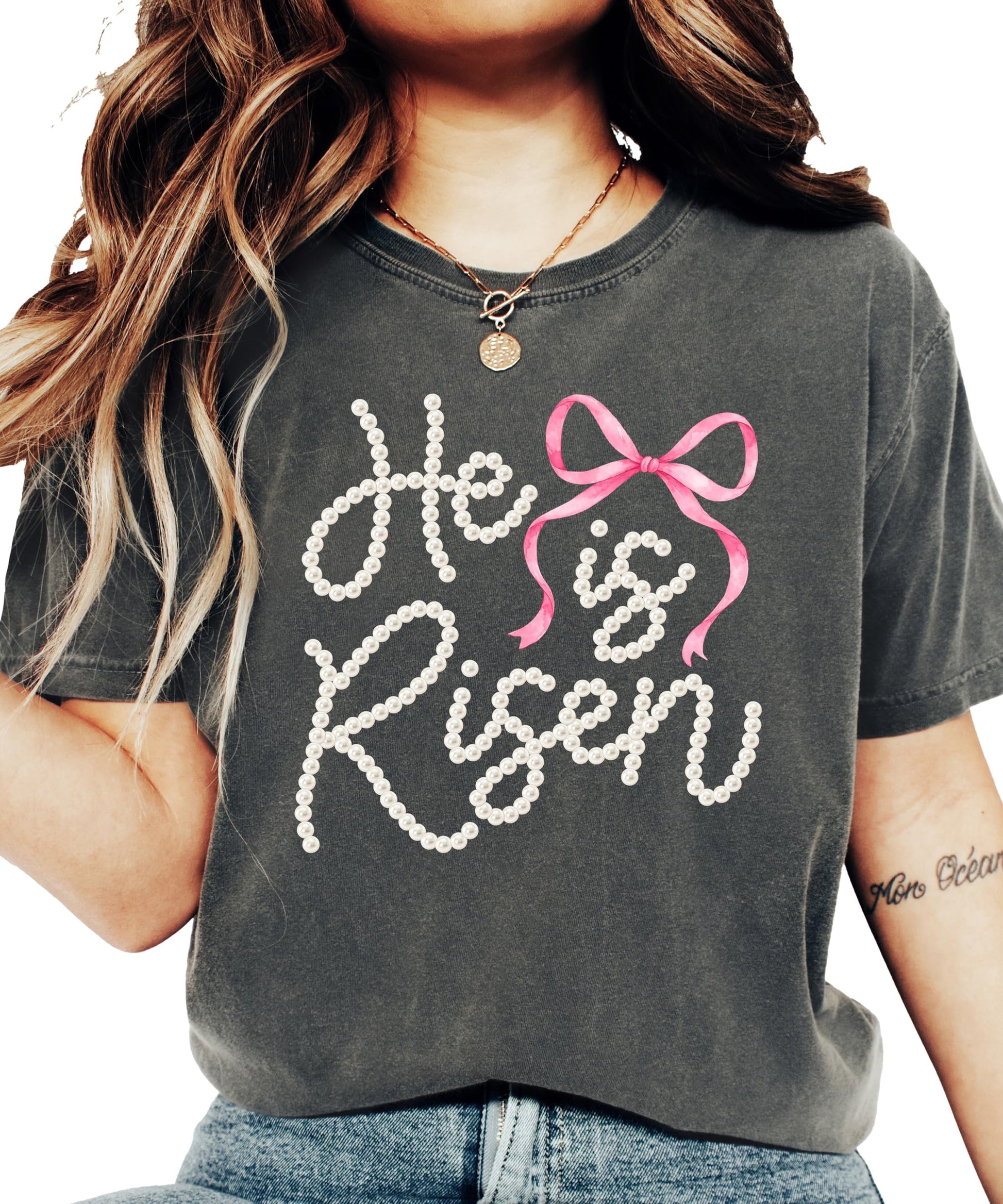 Women's He Is Risen Easter graphic tee with pearl-style lettering and pink coquette bow design