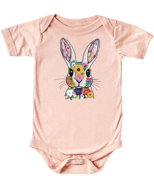 Close-up of floral rabbit ink print on a soft peach baby onesie