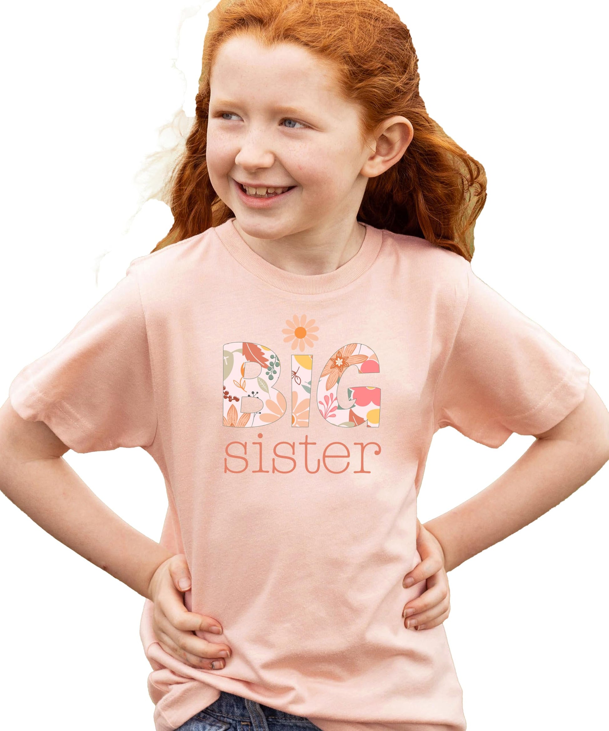Young girl smiling in a peach Big Sister graphic shirt, floral daisy design