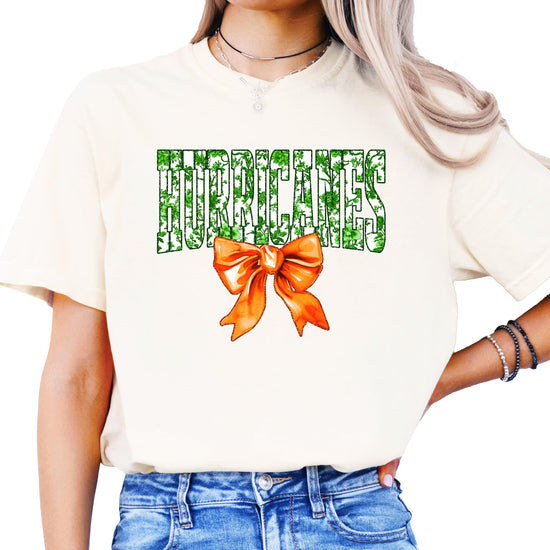 Close-up of green floral 'Hurricanes' graphic with vibrant orange bow on a women's ivory tee