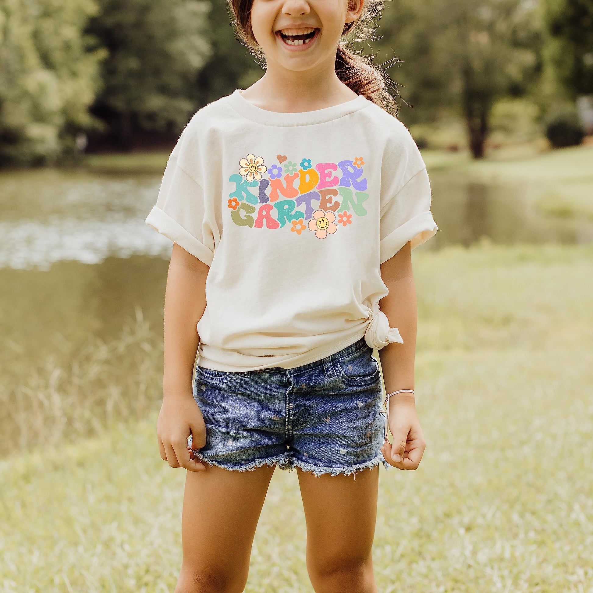 Youth girl wearing natural groovy daisy first day of school kindergarten graphic tee, styled flat lay