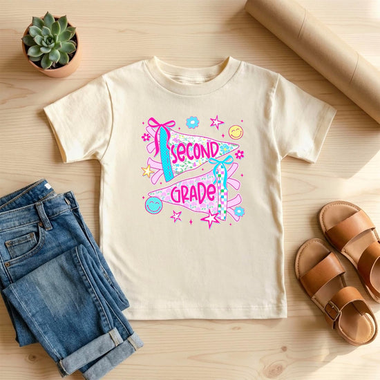 Flat lay of girls 2nd grade floral pennant tee in natural and pink colorways by Olive Loves Apple