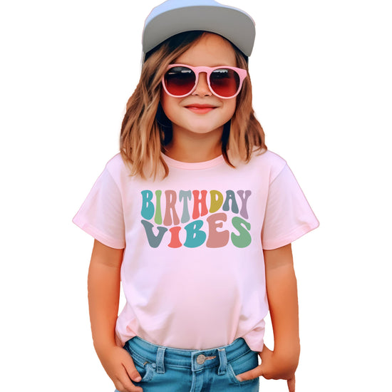 Toddler girl wearing Birthday Vibes shirt in white on peach for birthday outfit