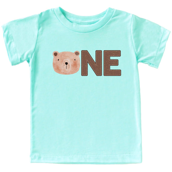 Baby boy wearing a natural color first birthday t-shirt with a bear face ONE graphic design