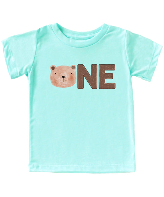 Baby boy wearing a natural color first birthday t-shirt with a bear face ONE graphic design