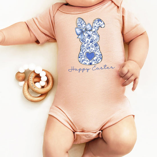 Flat lay of peach Easter baby one-piece bodysuit with blue floral bunny graphic