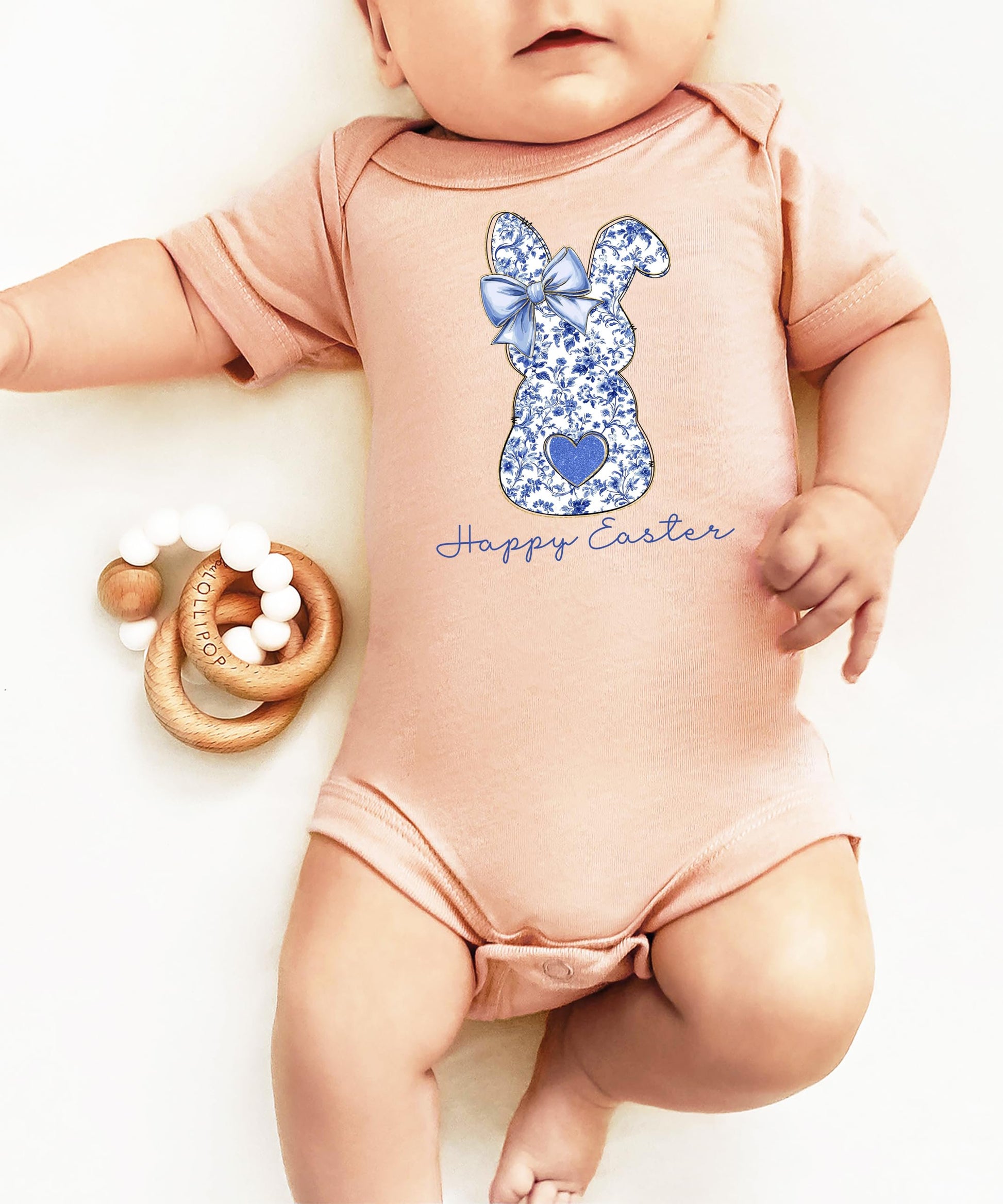 Flat lay of peach Easter baby one-piece bodysuit with blue floral bunny graphic