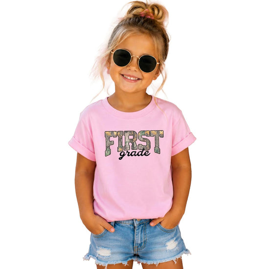 First Grade camo shirts in multiple colors — natural, pink, and military green kids tees