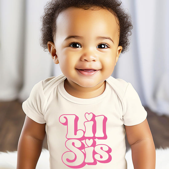 Flat lay of Lil Sis baby girl snap bodysuit with girly retro lettering on natural fabric