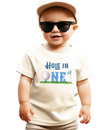Boys toddler natural tee with Hole in One golf-themed first birthday graphic featuring golf ball, flag, and grass design