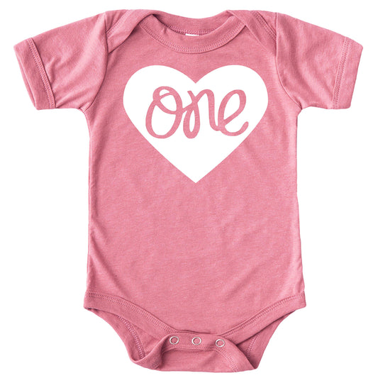 Close-up of One in a Heart first birthday bodysuit design on military green baby girl snap bodysuit