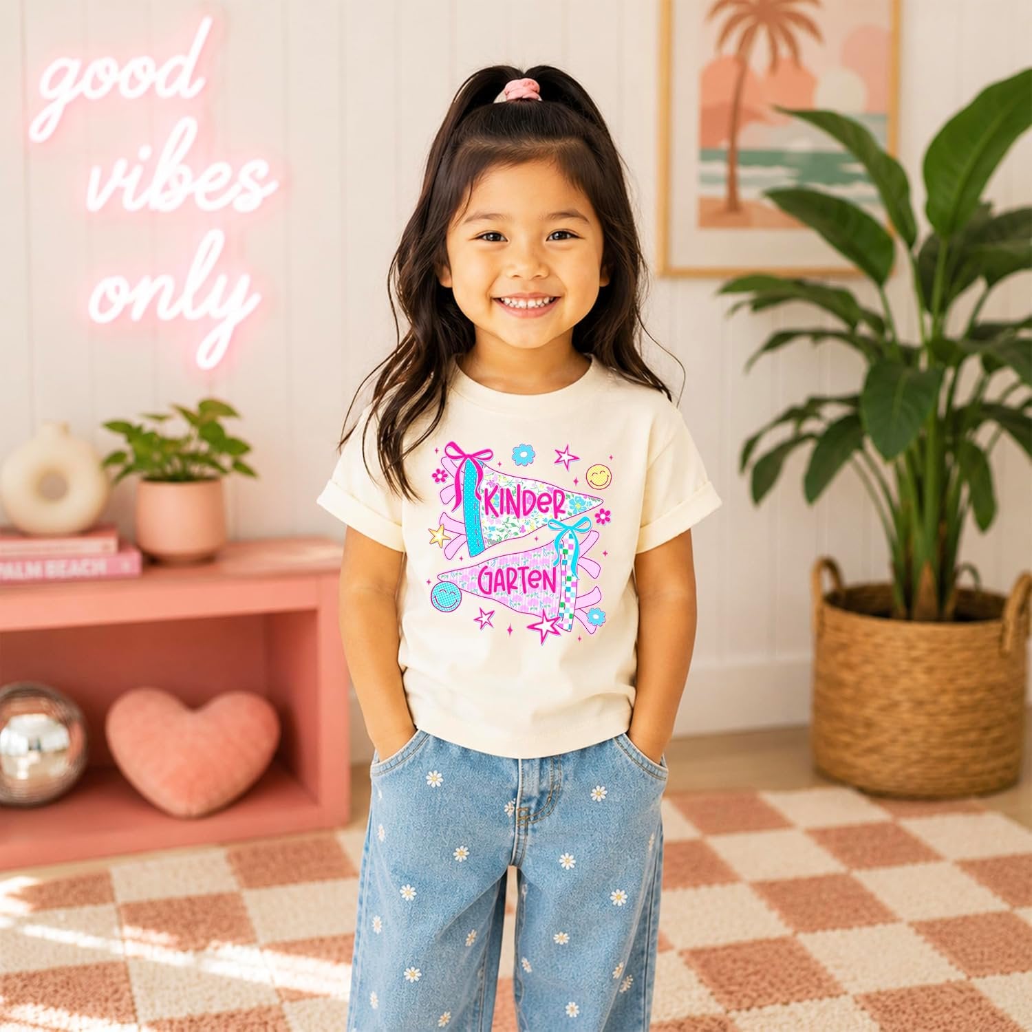 Close-up of kindergarten pennant graphic with checkered accents, retro daisies, and coquette bows on girls tee