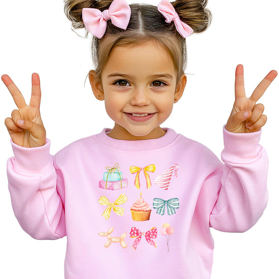 Pastel coquette birthday sweatshirt for kids with bow, cupcake, and balloon graphic in pink tones