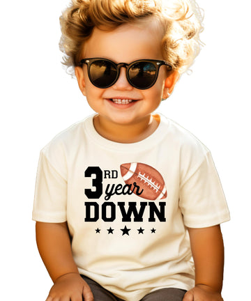 Flat lay of kids natural shirt with 3rd Year Down football birthday design