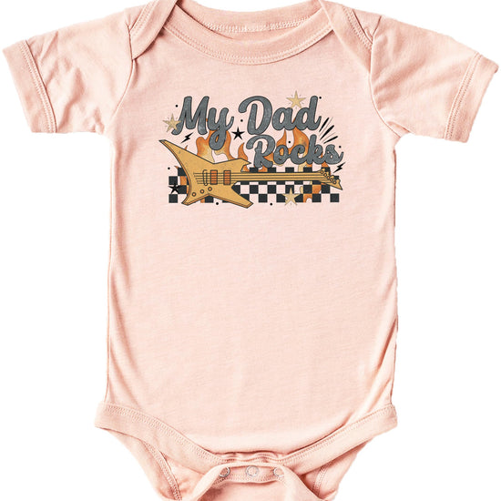 Flat lay of peach My Dad Rocks baby one-piece bodysuit with retro guitar art