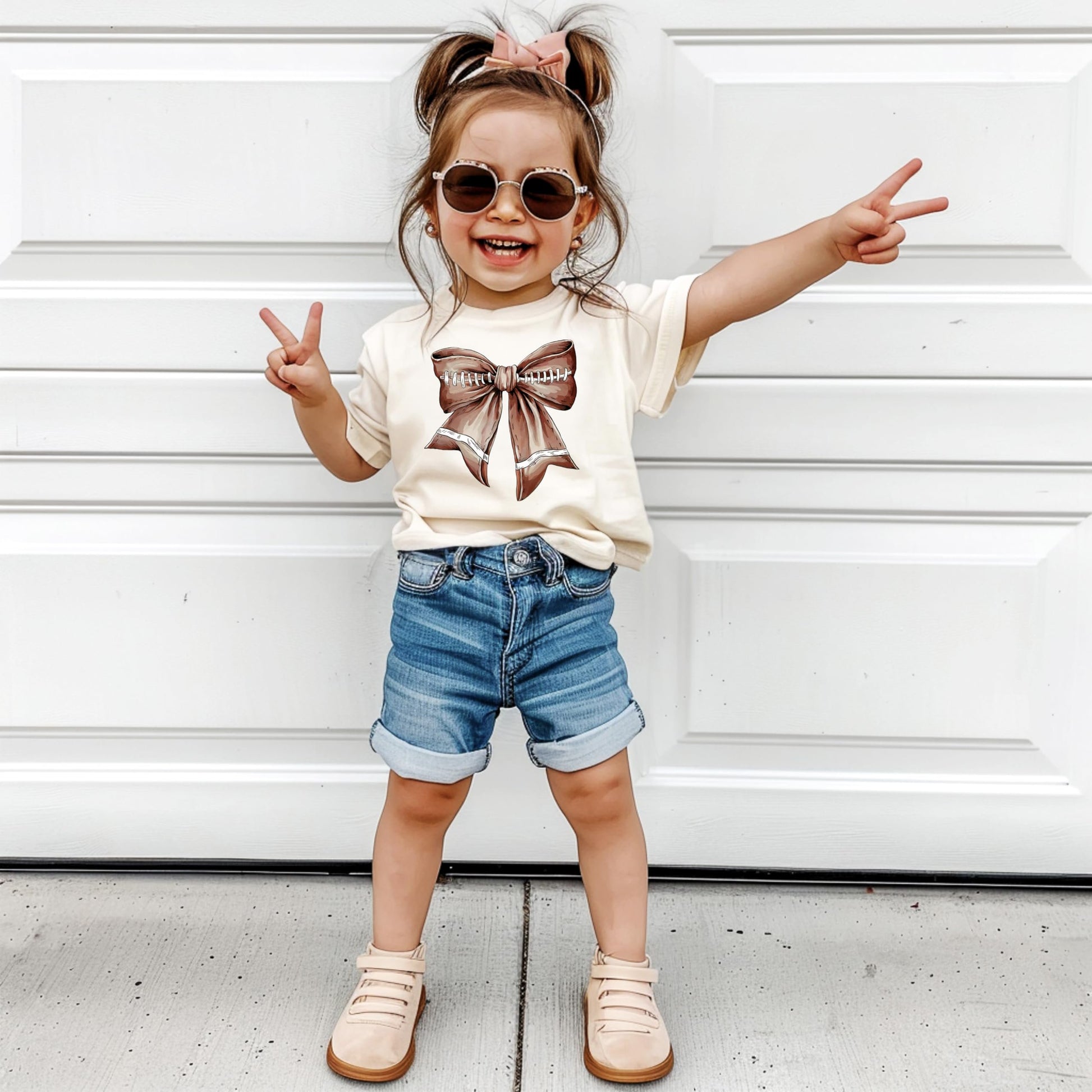 Flat lay of girly football bow t-shirt for toddlers and girls in natural fabric color