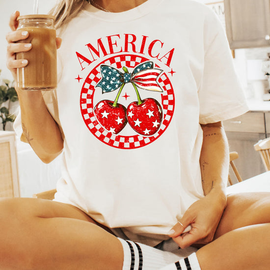 Flat lay of ivory patriotic tee featuring cherry with bow and stars design