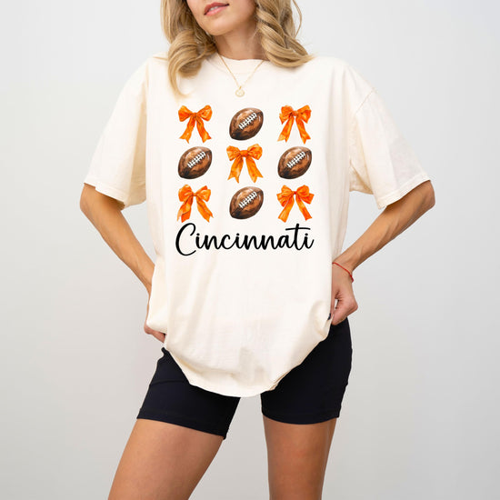 Close-up of orange bows and footballs graphic on ivory Cincinnati football shirt for women