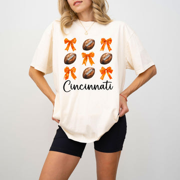 Close-up of orange bows and footballs graphic on ivory Cincinnati football shirt for women