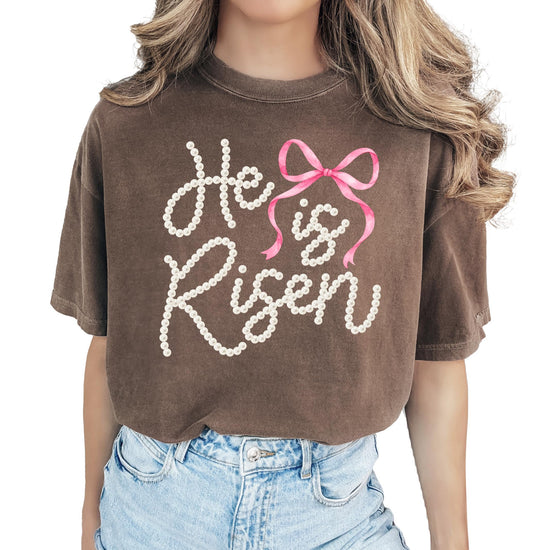 Close-up of He Is Risen pearl lettering and pink bow graphic print on women's Easter tee