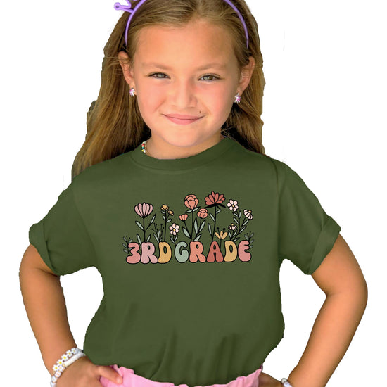 Young girl wearing military green 3rd grade floral back to school graphic tee, styled flat lay
