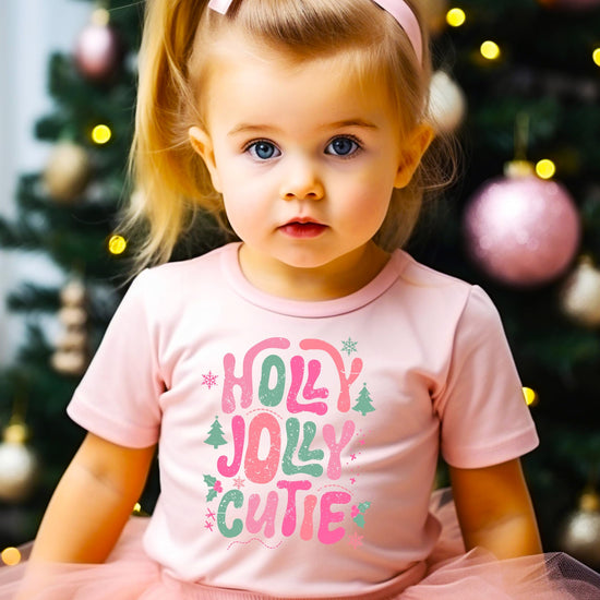 Flat lay of pink kids' Christmas graphic tee with holly jolly holiday design on light background