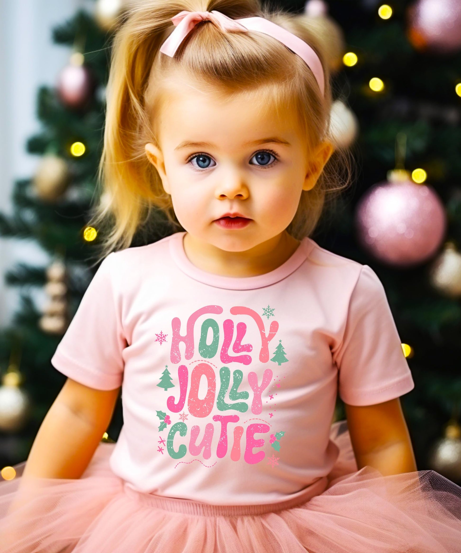 Flat lay of pink kids' Christmas graphic tee with holly jolly holiday design on light background