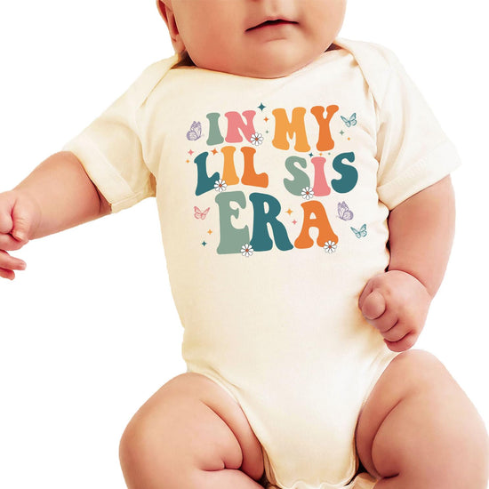 In My Lil Sis Era peach baby bodysuit with retro lettering, butterflies, and daisy floral design