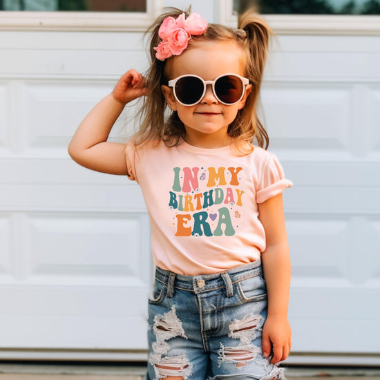 Close-up of 'In My Birthday Era' wavy lettering graphic print on peach youth tee