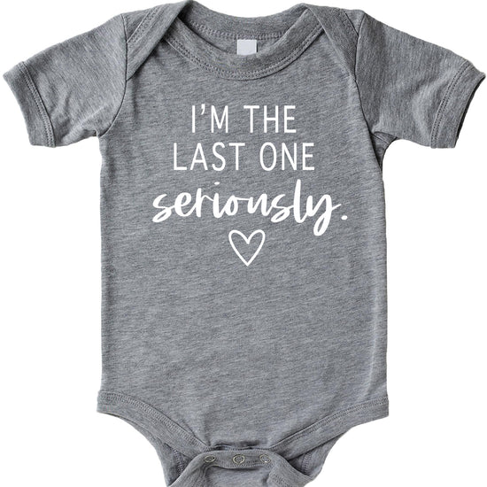 White graphic baby bodysuit on mauve background reading I'm The Last One Seriously — funny pregnancy reveal newborn outfit