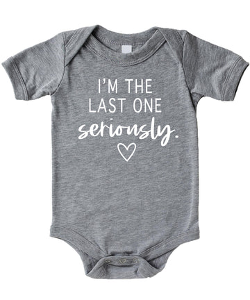 White graphic baby bodysuit on mauve background reading I'm The Last One Seriously — funny pregnancy reveal newborn outfit