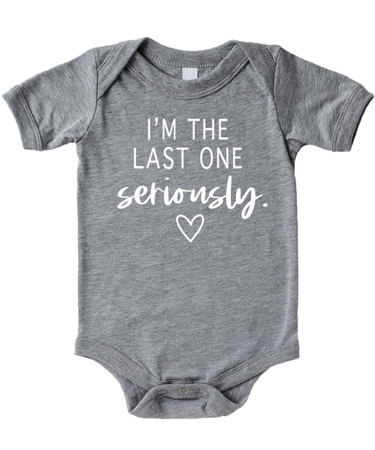 White graphic baby bodysuit on mauve background reading I'm The Last One Seriously — funny pregnancy reveal newborn outfit