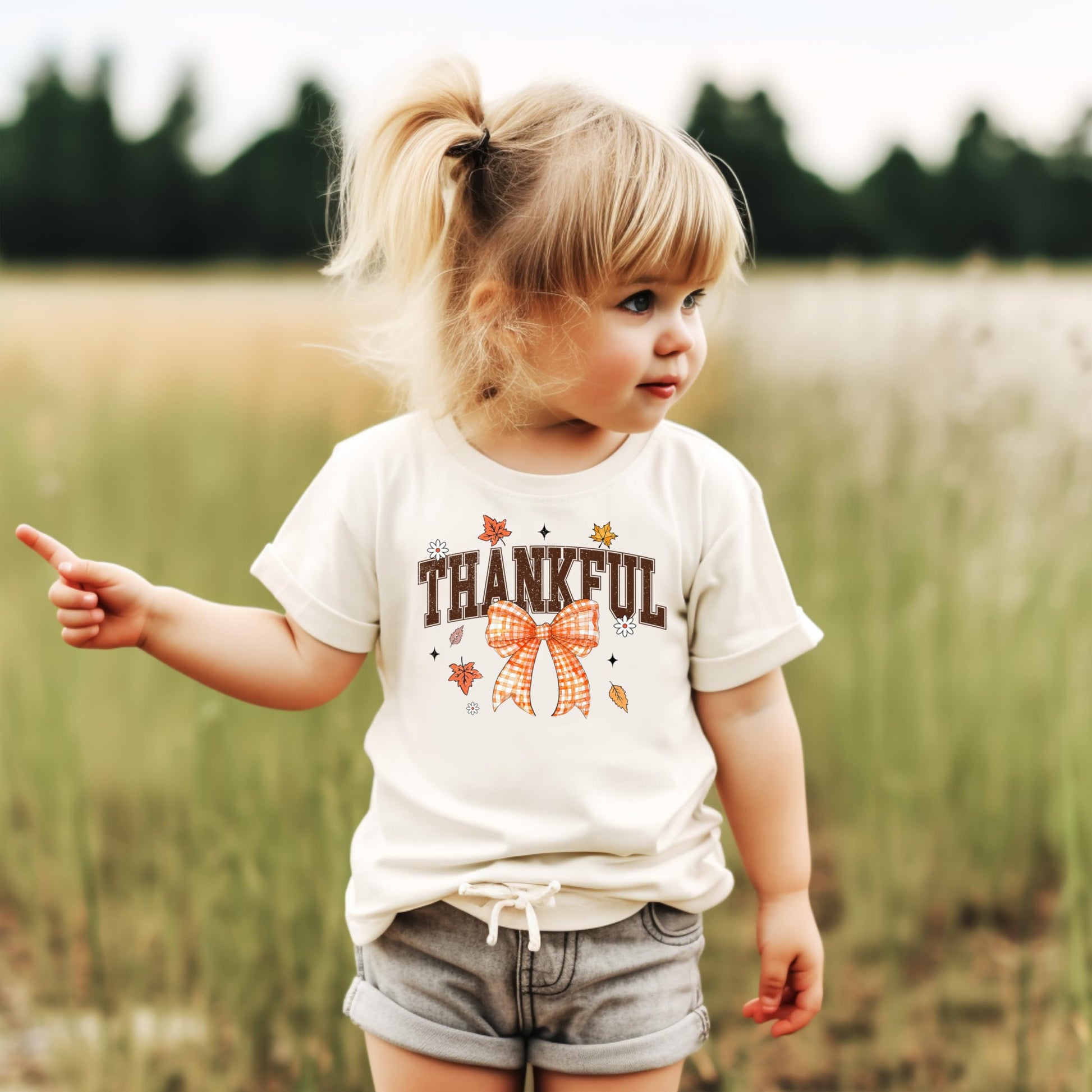 Orange Thankful kids shirt laid flat displaying autumn leaf and bow graphics