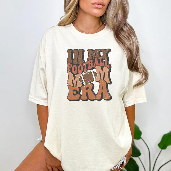 In My Football Mom Era ivory graphic tee displayed flat, showing full shirt design