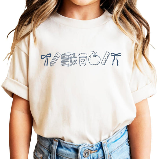 Pink coquette bow back to school graphic tee featuring hand-drawn school supplies including books, pencil, apple, and ruler