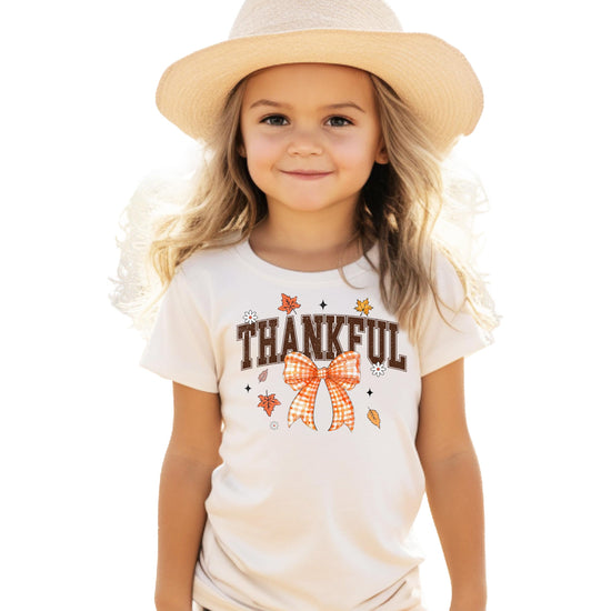 Close-up of orange Thankful text with decorative gingham bow graphic on kids tee