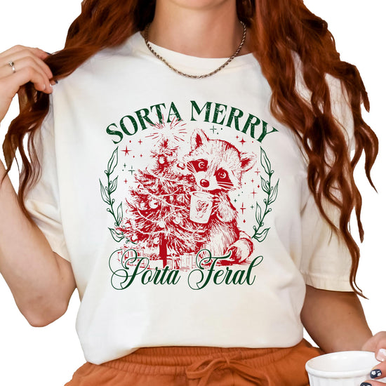 Close-up of Sorta Merry Sorta Feral raccoon holiday print on ivory women's graphic tee