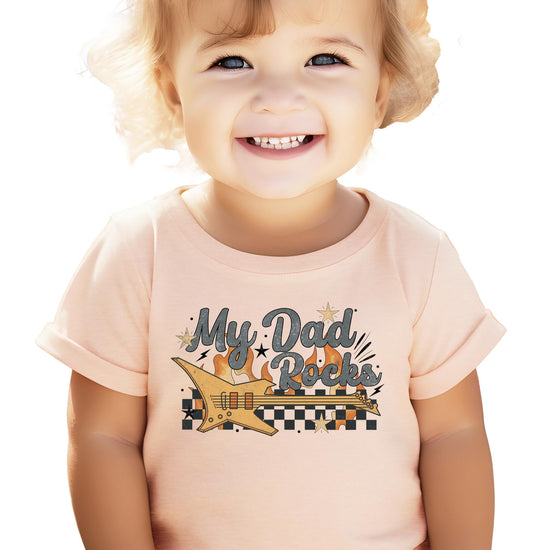 Flat lay of My Dad Rocks peach kids' tee with bold rocker graphic design