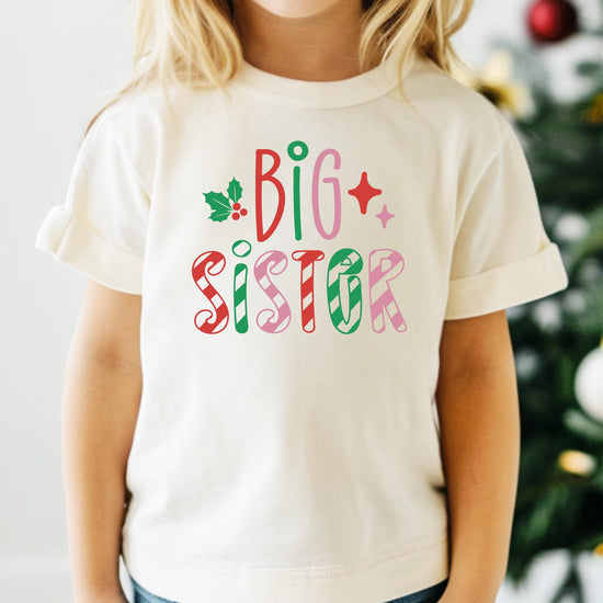 Front view of festive big sister Christmas shirt with colorful candy cane stripes for girls