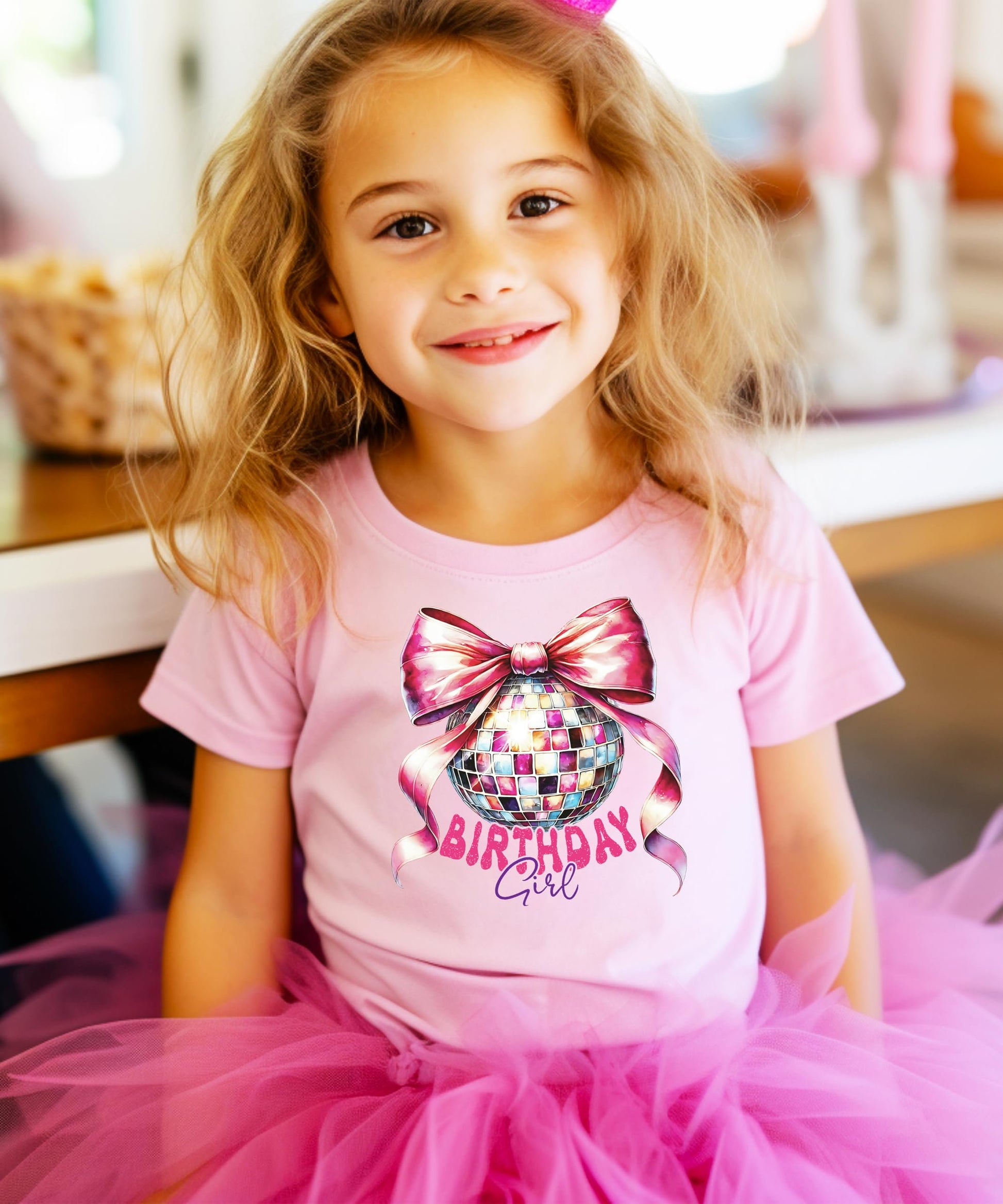 Detail shot of vibrant pink bow and disco ball graphic on kids birthday girl graphic tee