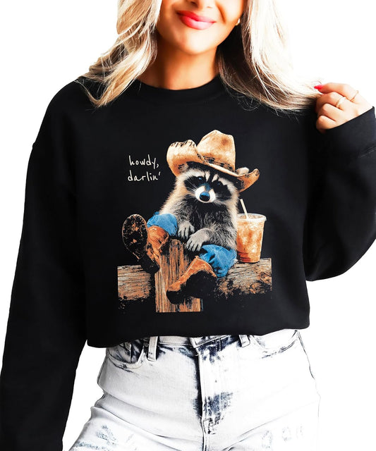 Funny cowboy raccoon crewneck sweatshirt in black with 'Howdy' graphic — raccoon in cowboy hat holding iced coffee