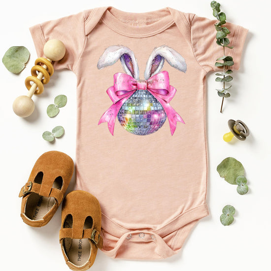 Flat lay of peach baby bodysuit with Easter disco bunny graphic — bunny ears and pink bow spring design